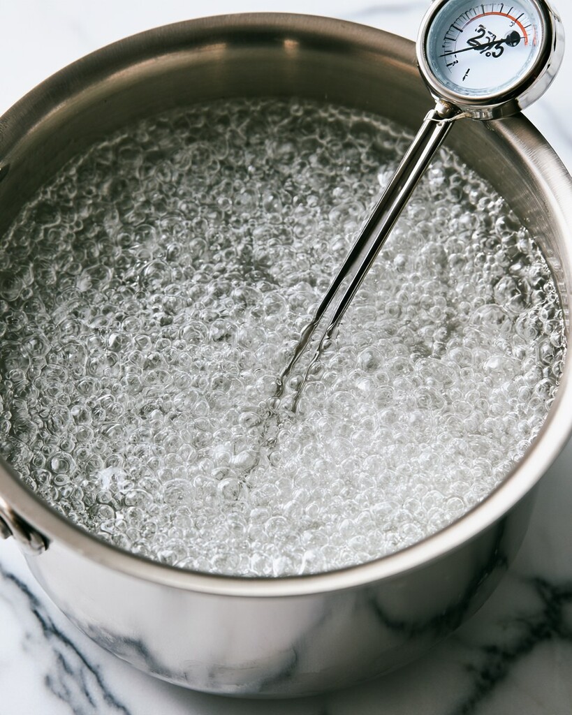 Allulose syrup bubbling vigorously in a metal saucepan with a candy thermometer attached