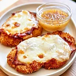 One-Pan Malibu Chicken with Hot Honey Mustard Golden breaded chicken breast topped with melted Swiss cheese and smoked ham on a white plate beside mustard sauce