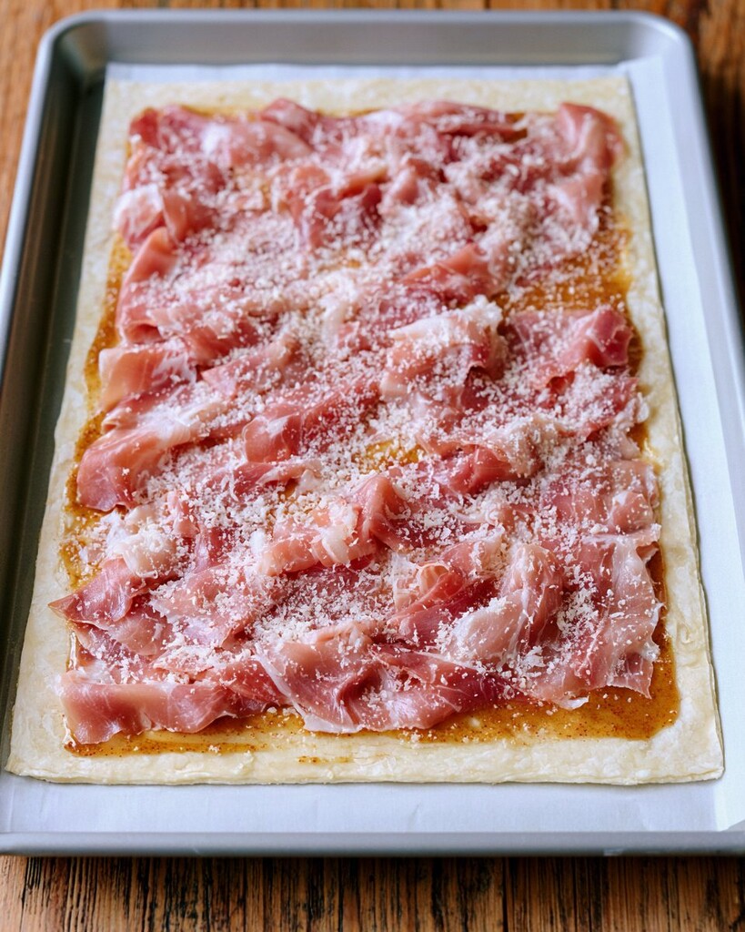 Sliced ham and grated cheese layered over a mustard spread on a sheet of puff pastry.