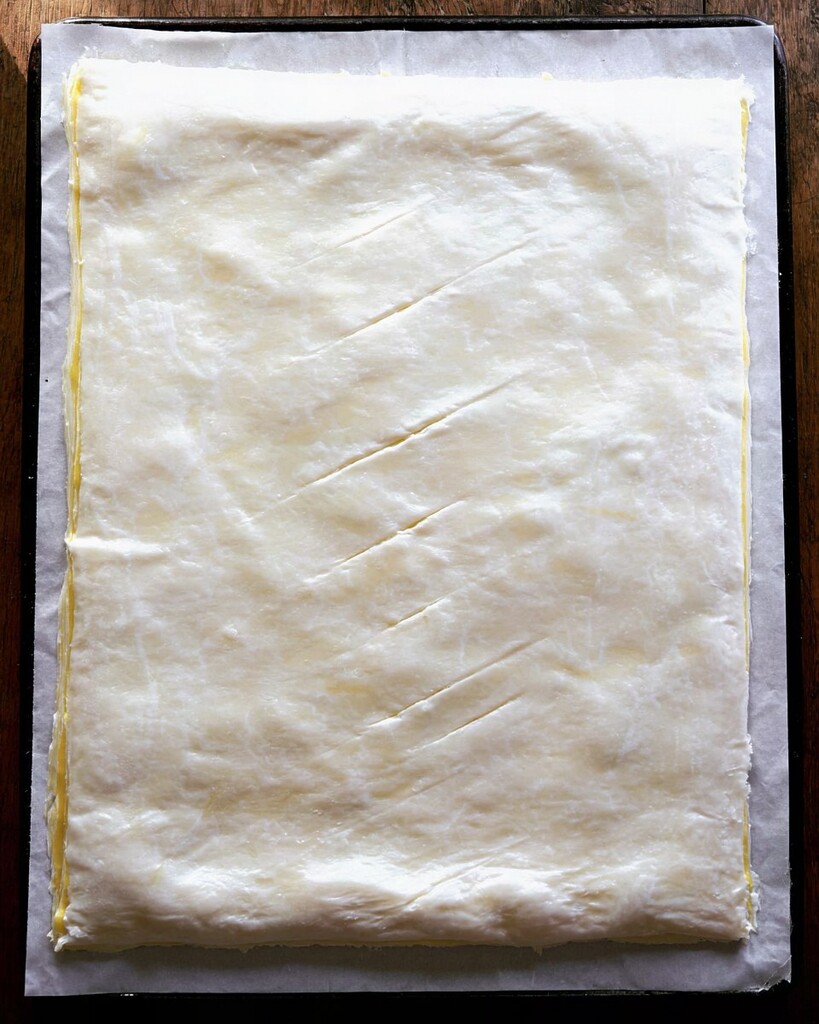 Two sheets of puff pastry sealed at the edges with diagonal slits cut across the top layer.
