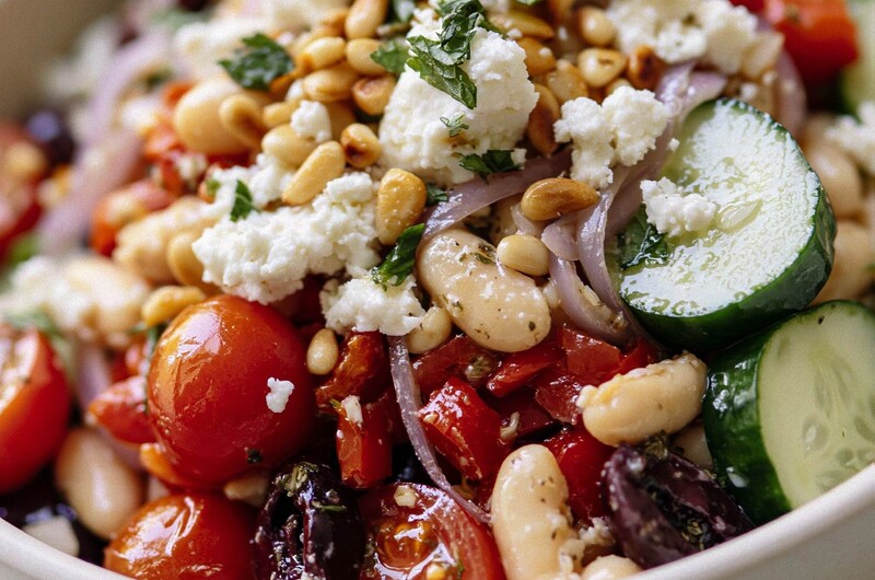 Finished Greek white bean salad served in a ceramic bowl with crumbled feta and pine nuts