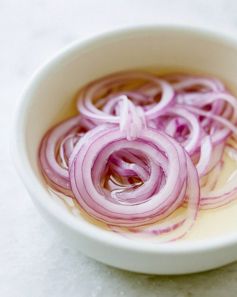 Thinly sliced red onions soaking in golden lemon juice inside a white bowl