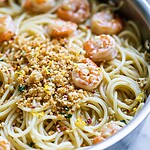 Spaghetti tossed in a garlic butter sauce inside a skillet topped with pink shrimp and toasted panko