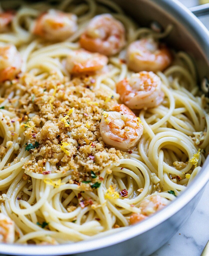Spaghetti tossed in a garlic butter sauce inside a skillet topped with pink shrimp and toasted panko