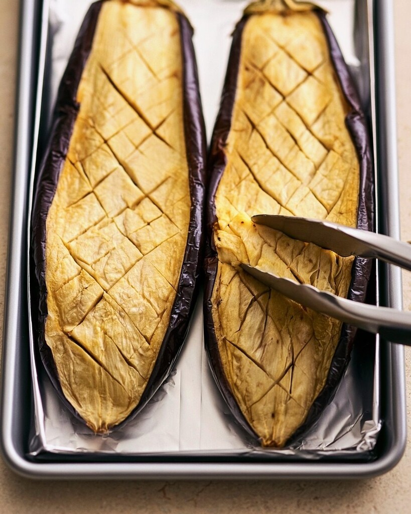 Roasted eggplant halves looking shriveled and soft on a baking sheet