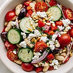 Fully assembled Greek white bean salad mixed with fresh vegetables, crumbled feta, and toasted pine nuts