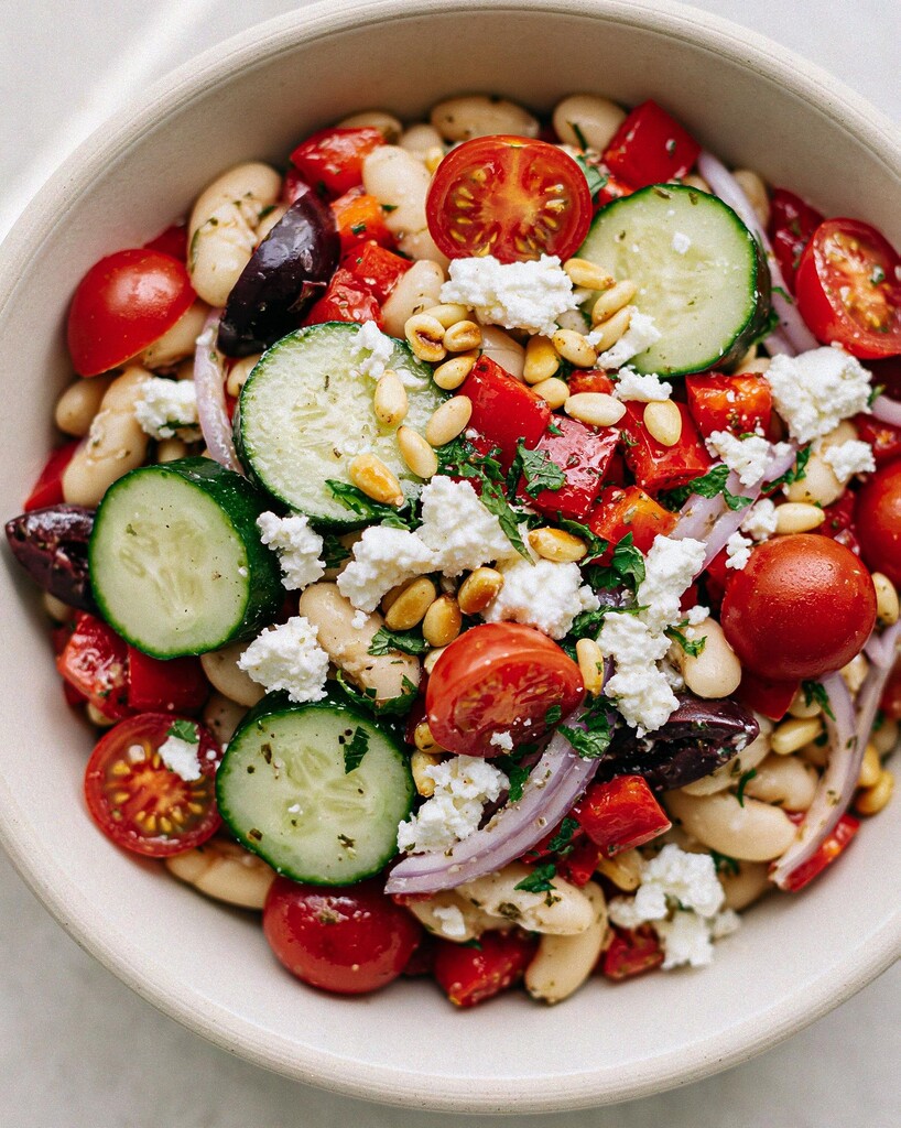 Fully assembled Greek white bean salad mixed with fresh vegetables, crumbled feta, and toasted pine nuts