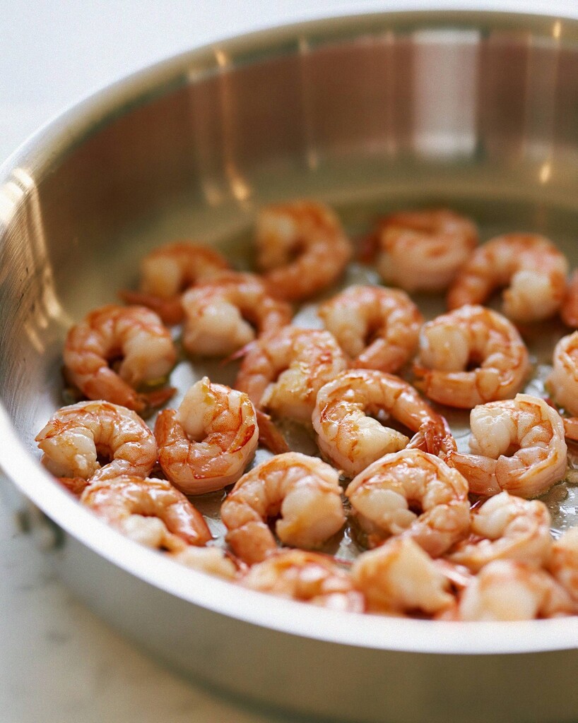 Pink peeled shrimp searing in a single layer inside a wide metal pan