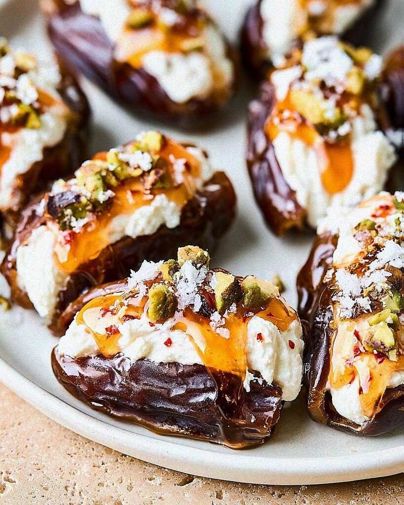 Close up of hot honey glistening over crushed pistachios and flaky sea salt on a stuffed date