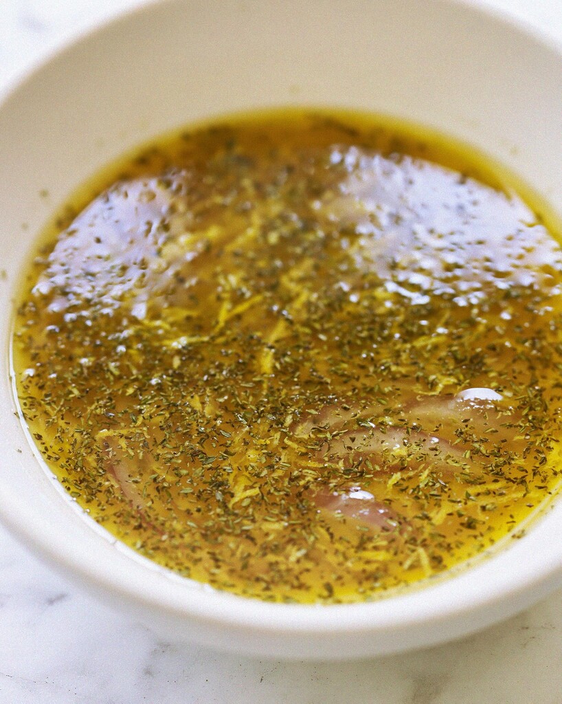 Golden salad dressing mixed with herbs and soaked red onions in a white bowl
