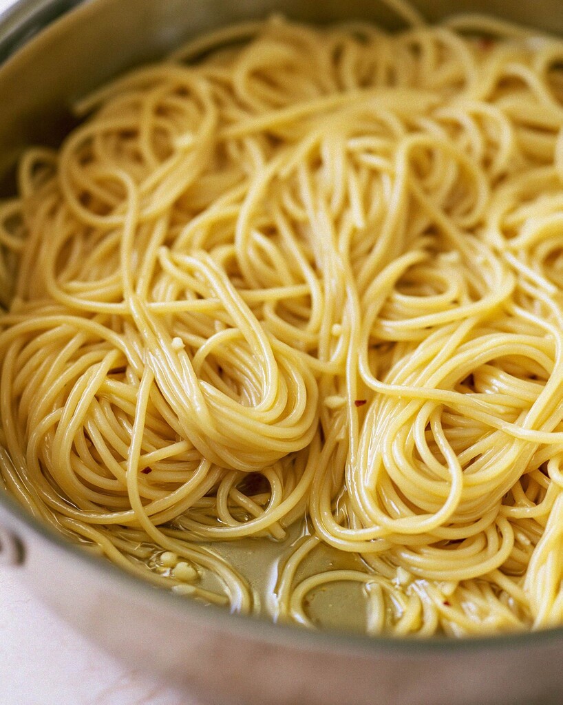 Spaghetti noodles simmering and softening in a shallow starchy liquid in a large skillet