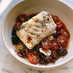 15-Minute Mediterranean Baked White Fish in One Pan A tender portion of baked white fish resting in a ceramic bowl, surrounded by blistered cherry tomatoes, Kalamata olives, and fresh dill