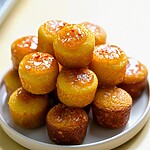 Golden mini cornbread bites stacked on a white plate, topped with a shiny glaze and coarse salt