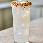 Toasted Coconut Vodka Lime Crush A tall glass of coconut lime vodka crush with a toasted coconut rim, surrounded by ice and a lime wedge