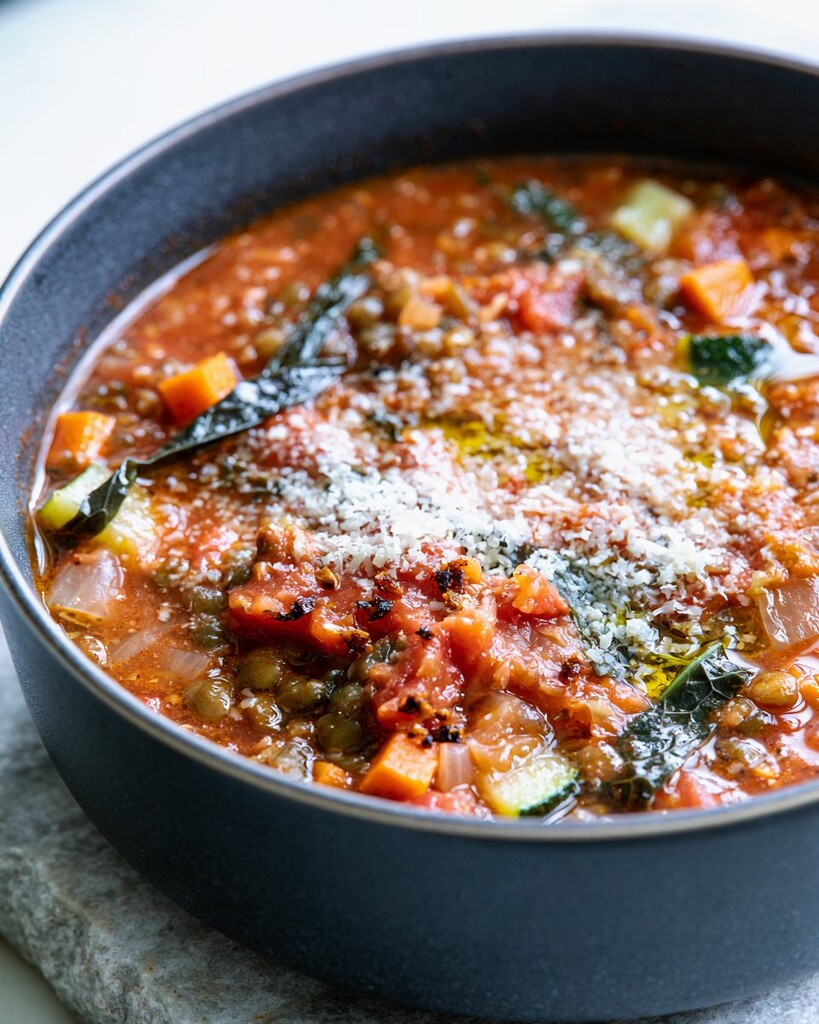 Thick Italian lentil soup in a black bowl with grated parmesan and oil