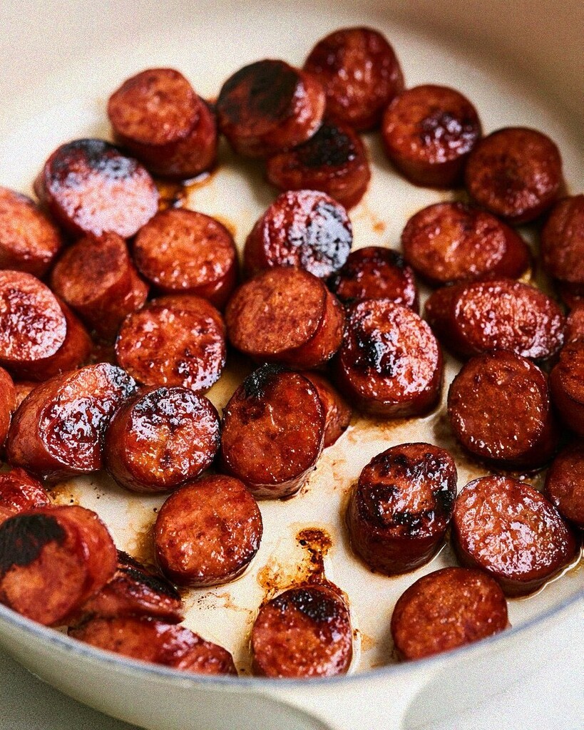 Sliced smoked sausage browning in a light-colored pot