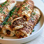 A stack of baked golden brown taco sticks on a light plate, showing browned edges and melted cheese.
