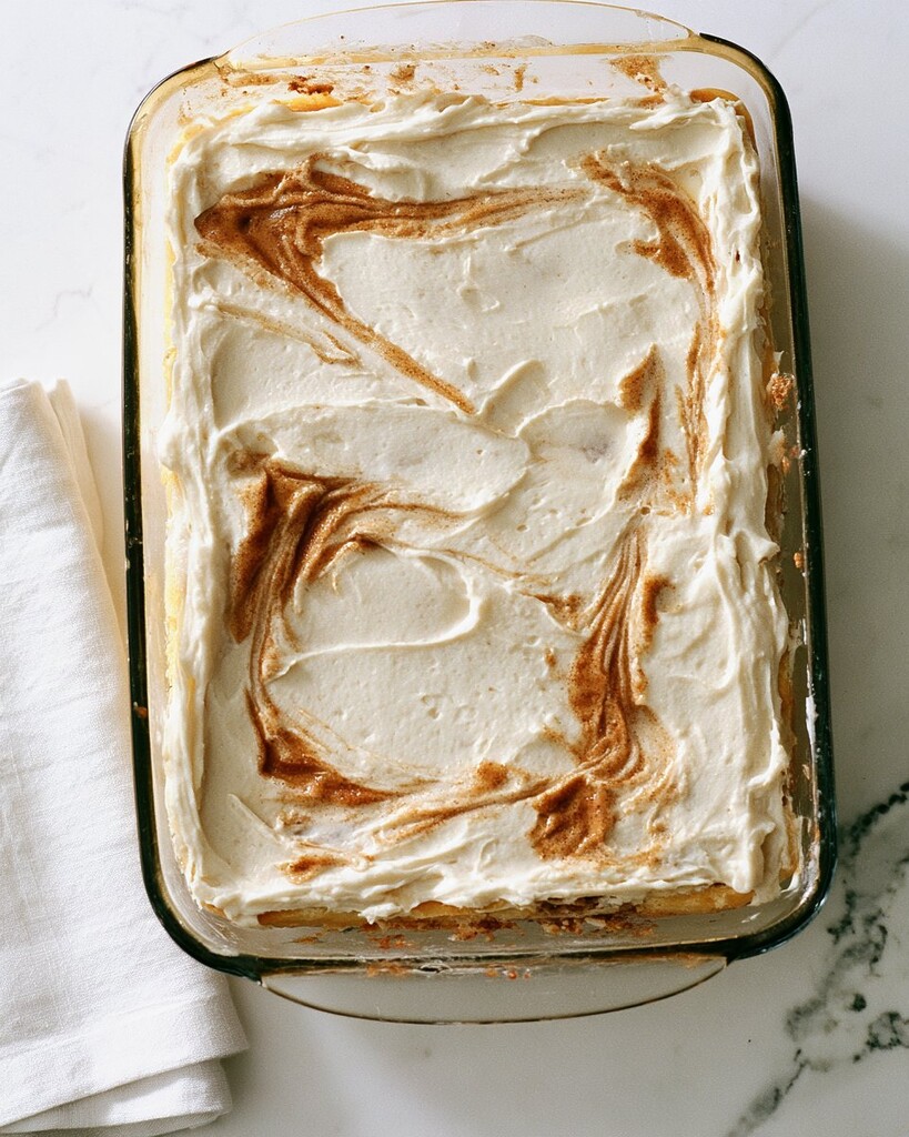 A 9x13 glass pan holding a frosted cake with brown cinnamon swirls across the top