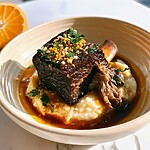 Plated bourbon-braised beef short ribs resting on a creamy puree, topped with brown sauce and green orange gremolata.