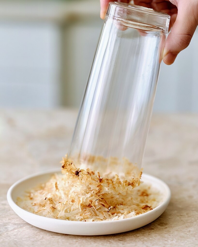 A tall glass being dipped into a plate of lightly toasted shredded coconut