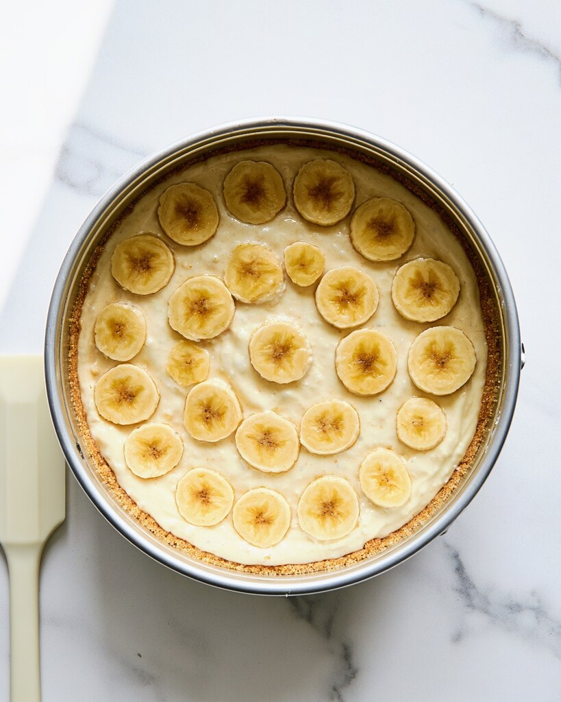 Sliced banana coins arranged over cheesecake batter inside a springform pan