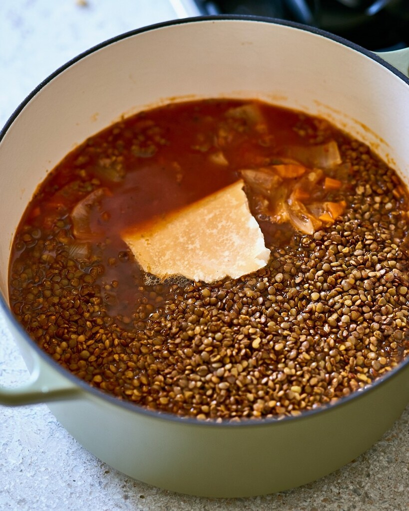 Brown lentils, a parmesan rind, and crushed tomatoes cooking in a heavy pot