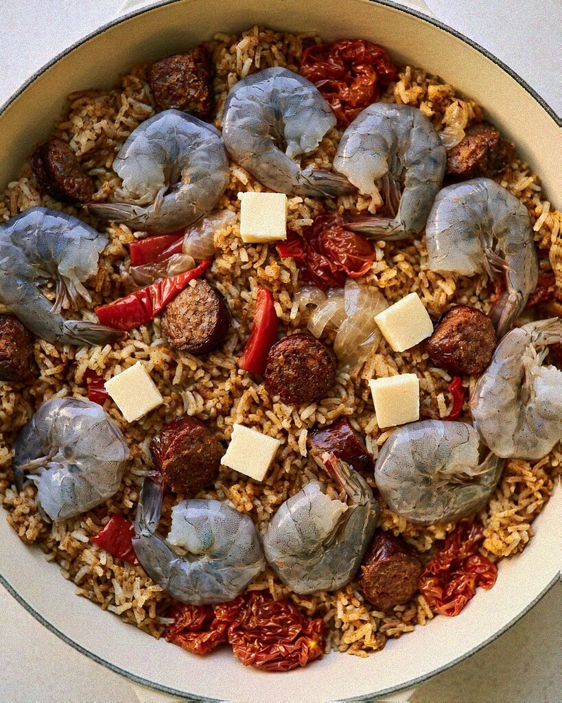 Raw shrimp and small cubes of butter arranged over cooked sausage and rice