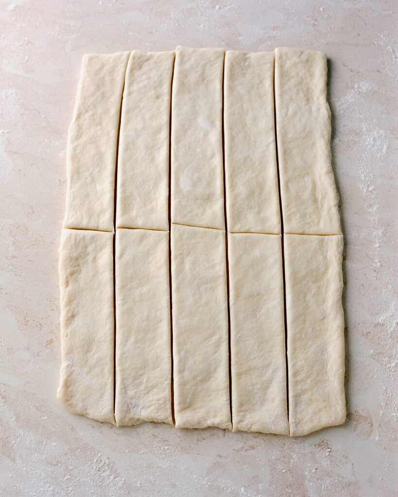 Ten equal rectangles of raw pizza dough cut on a floured surface.