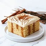 Gooey Cinnamon Roll Poke Cake (No Kneading Required) A square slice of cinnamon roll poke cake on a white plate revealing dark cinnamon filling inside the crumb