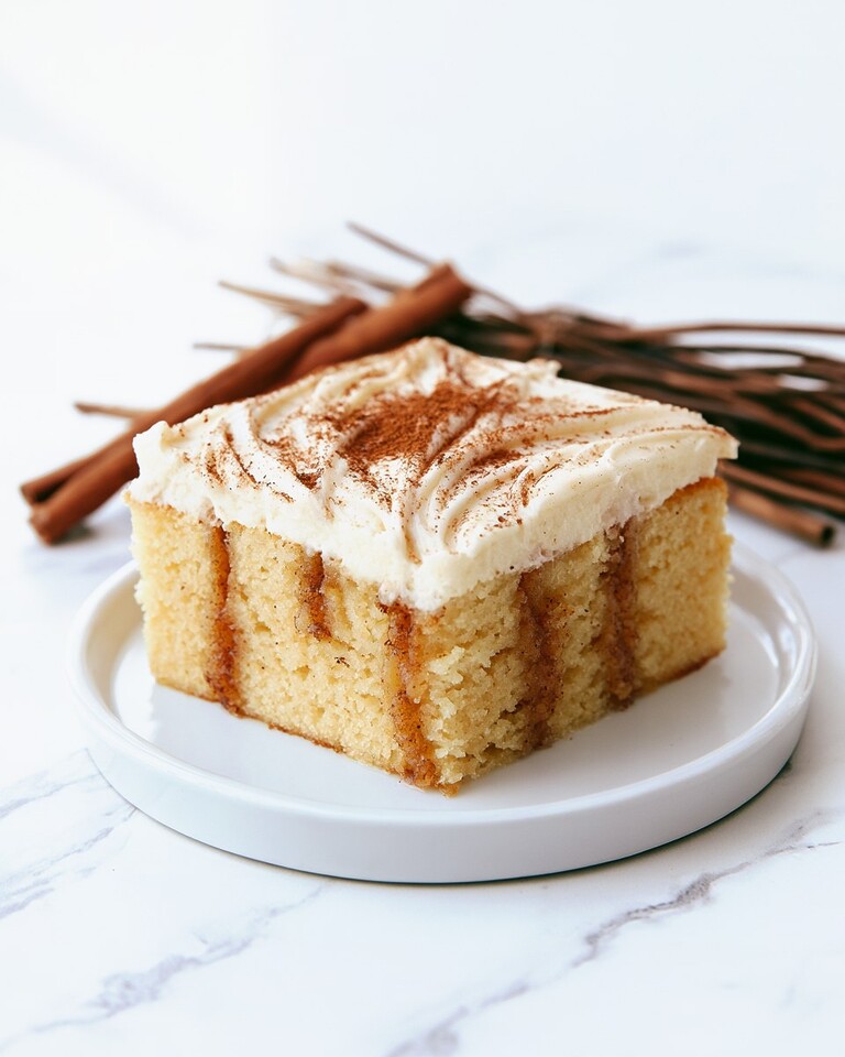 Gooey Cinnamon Roll Poke Cake (No Kneading Required) A square slice of cinnamon roll poke cake on a white plate revealing dark cinnamon filling inside the crumb