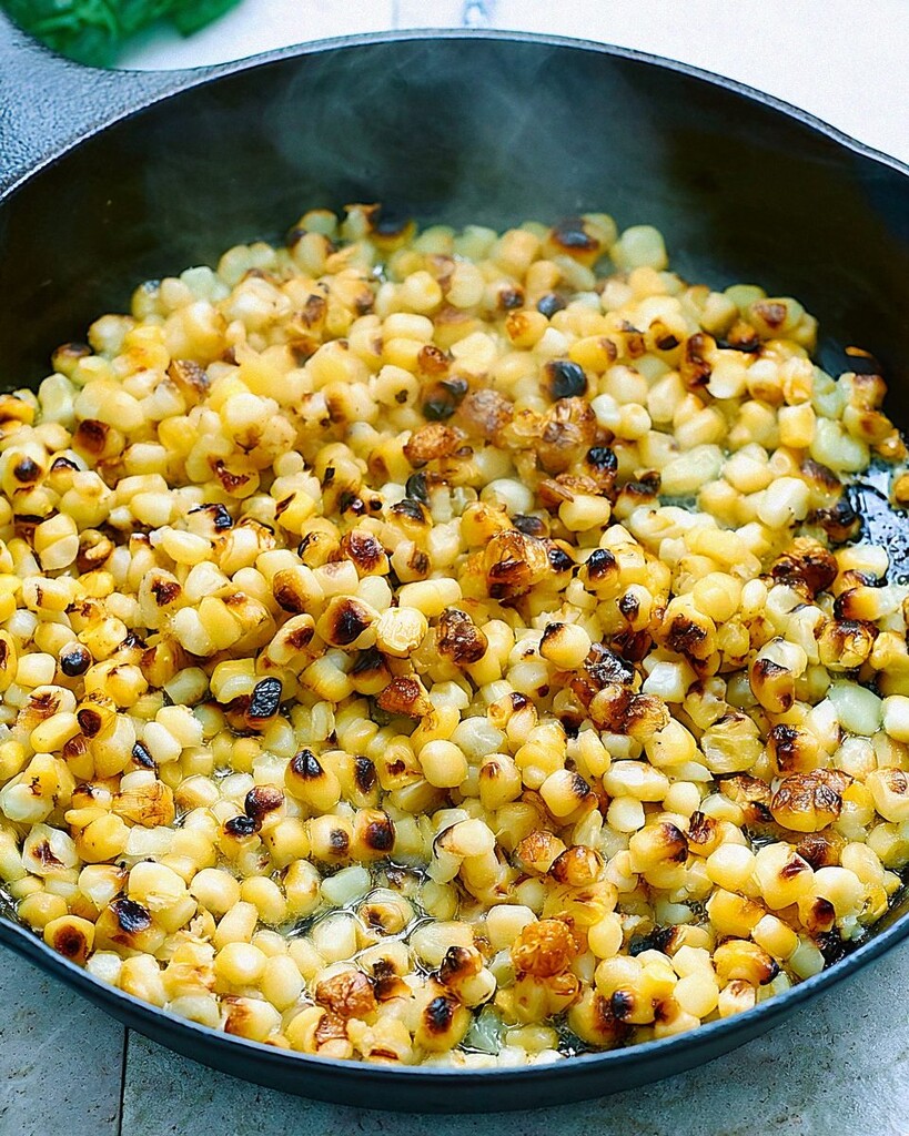 Yellow corn kernels blistering in a black cast-iron skillet until dark spots appear