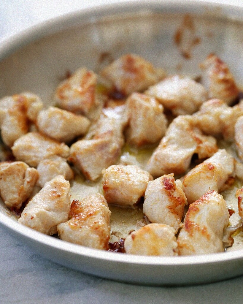 Cubed chicken browning in a metal skillet with a light golden crust.