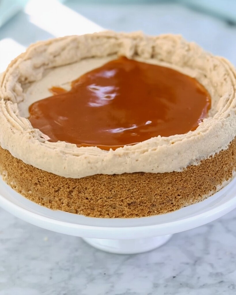 A single cake layer topped with a piped frosting border and filled with glossy cookie butter