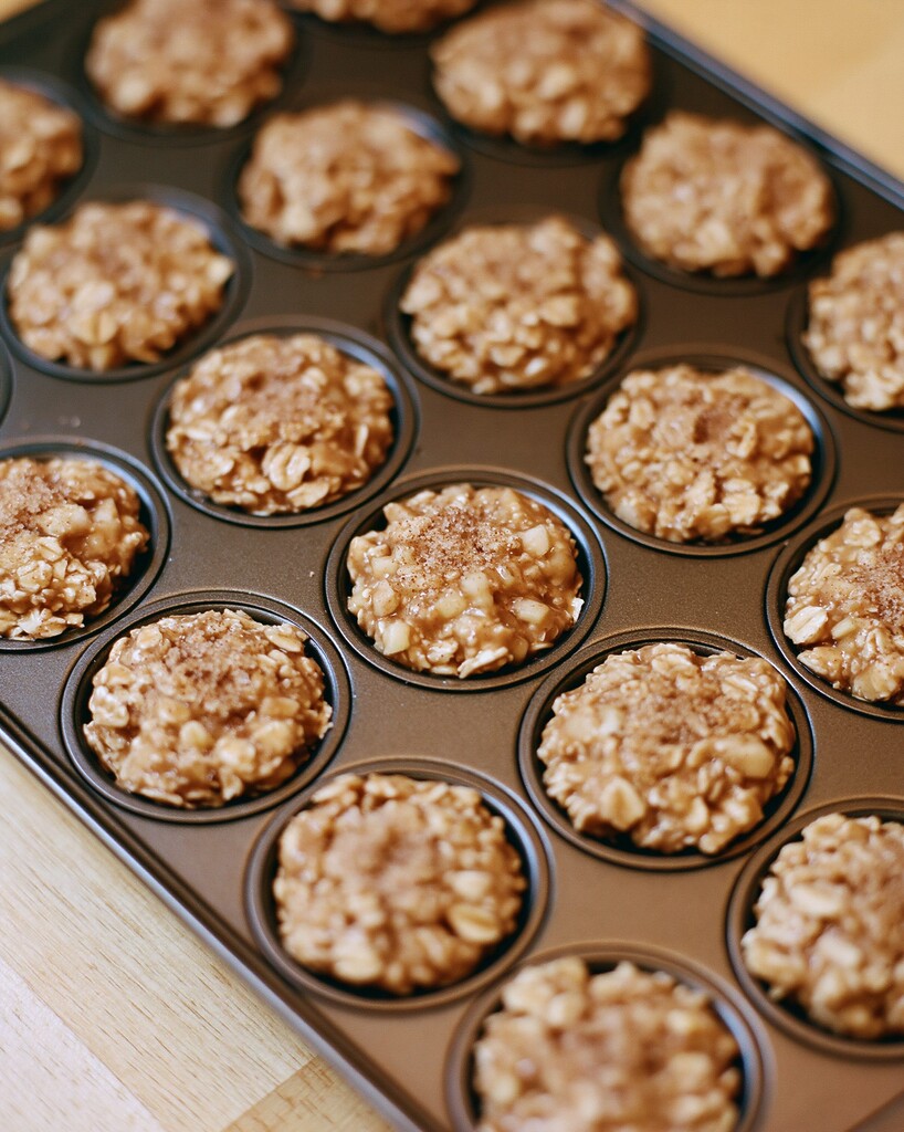 Unbaked oatmeal batter portioned into a mini muffin pan and topped with coarse sugar and cinnamon