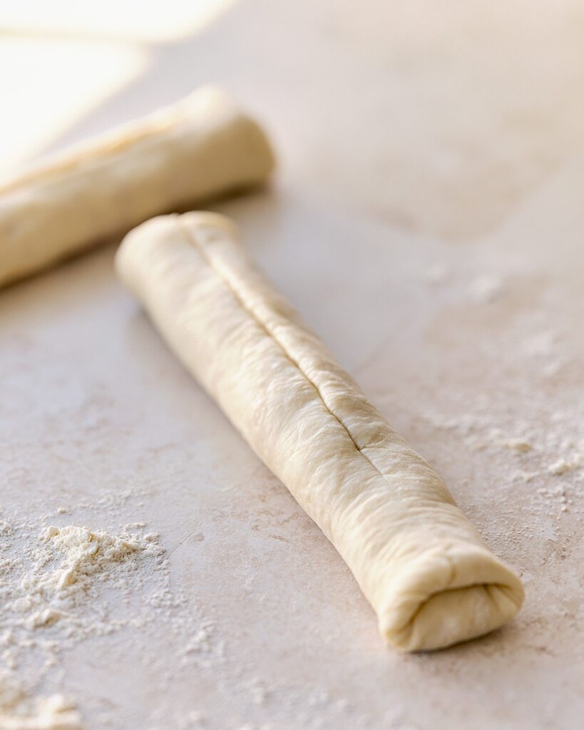 Raw pizza dough being folded over the taco meat and cheese filling into a cylinder.