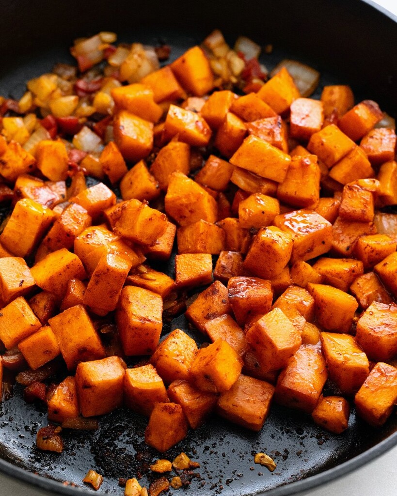 Cubed sweet potatoes cooking with peppers and onions in a skillet