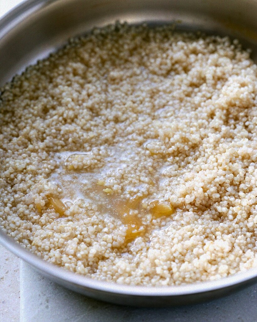 White quinoa simmering in bubbling chicken broth inside a skillet.