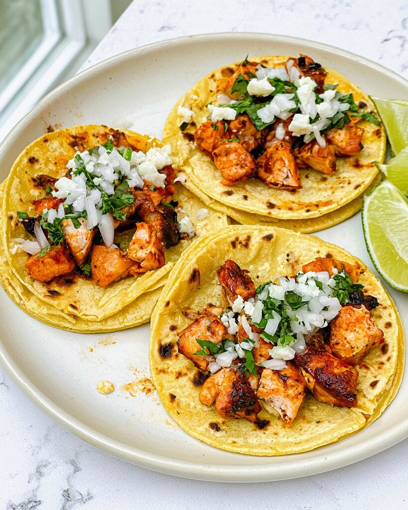 Three skillet-crisped chicken street tacos in double-stacked corn tortillas with onion, cilantro, and lime wedges