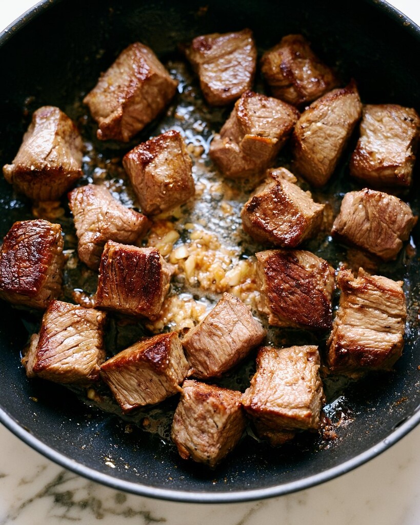 Cubed steak seared with minced garlic in a black skillet