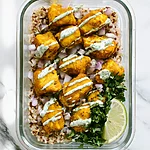 20-Minute Curried Chicken Meal-Prep Bowls Glass bowl holding golden curried chicken over rice with cilantro-lime yogurt sauce and red onions