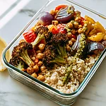 Sheet-Pan Roasted Veggie & Chickpea Bowls for Easy Lunches Glass meal prep bowl holding brown rice topped with roasted broccoli, bell peppers, onions, chickpeas, and a drizzle of pesto