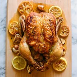 Garlic herb roast chicken resting on a wooden board next to lemon halves
