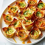 Golden baked wonton cups on a white plate drizzled with hot honey and topped with scallions