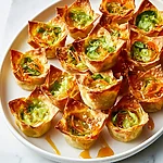Crispy Hot Honey Cabbage Dumpling Cups Golden baked wonton cups on a white plate drizzled with hot honey and topped with scallions