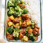 One-Pan Sweet Chili Chicken Meal Prep Bowls Glass bowl filled with sweet chili chicken, pineapple chunks, broccoli florets, and coconut rice