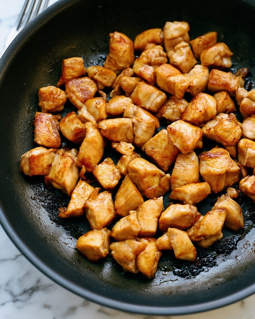 Diced chicken browning in a wide skillet
