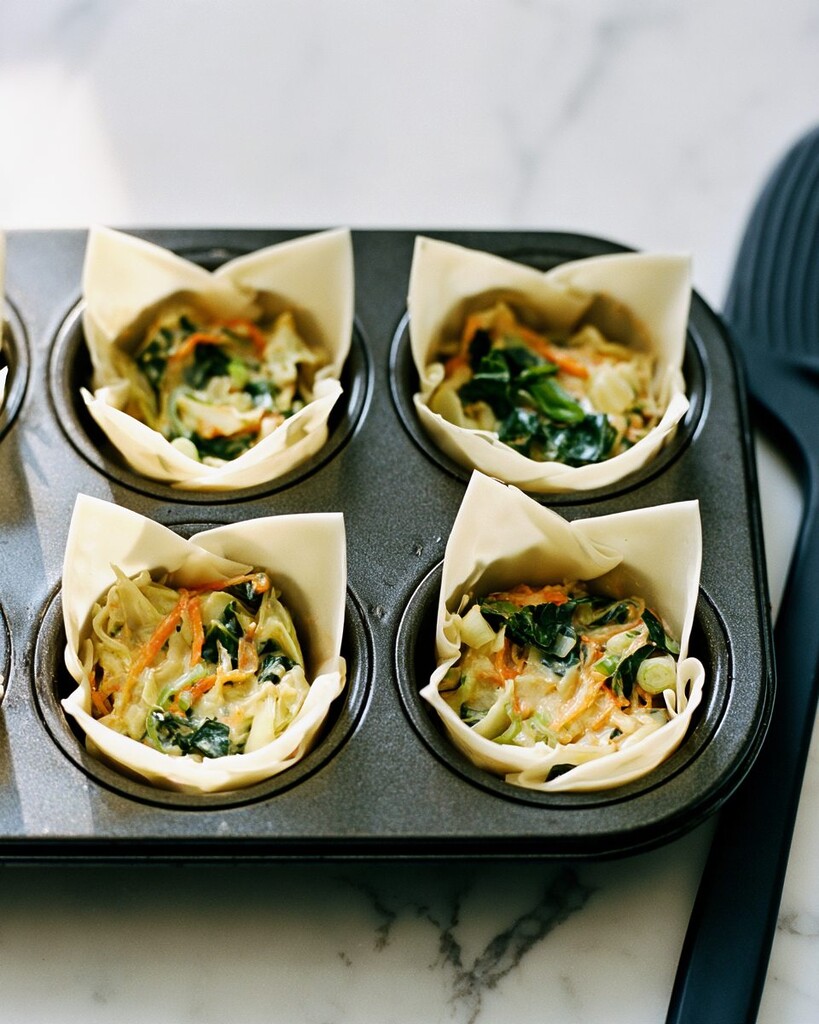 Raw wonton wrappers pressed into a muffin tin and filled with vegetable mixture