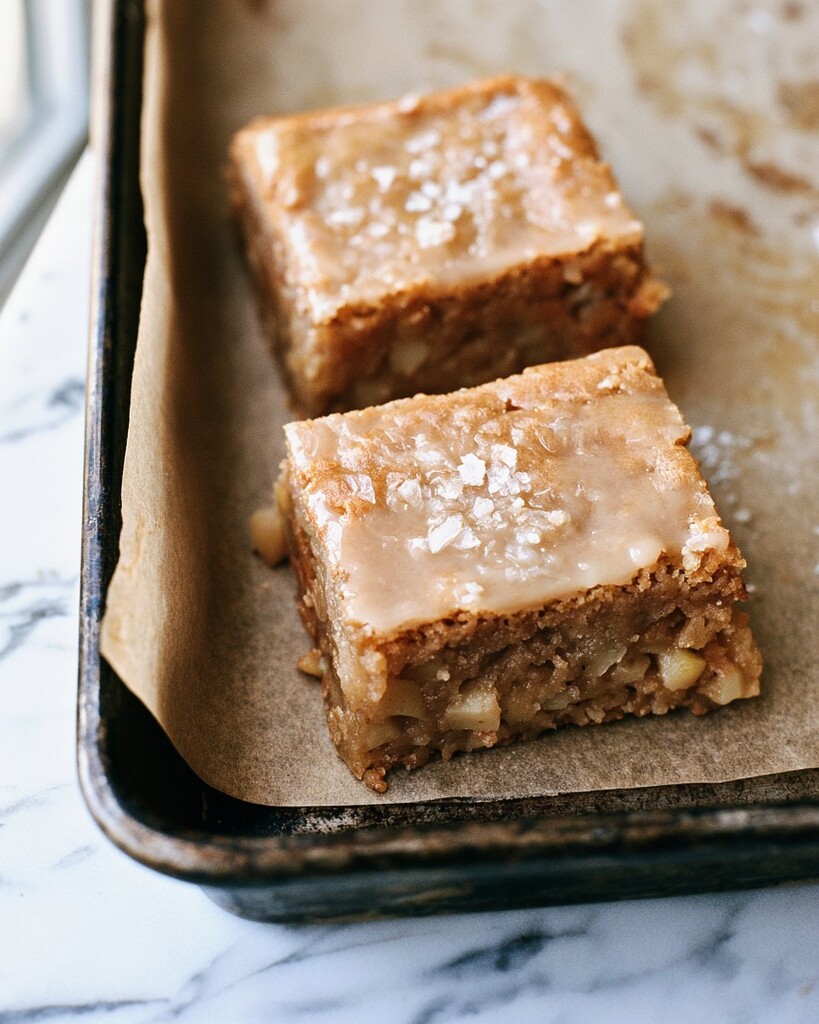 Two pieces of glazed apple blondies sitting inside a parchment-lined baking pan