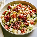 Italian grinder tortellini salad served in a ceramic bowl with mozzarella, cured meats, and red pepper flakes