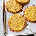 Lifting a baked polenta bite off the parchment paper with a metal spatula to show the thin crisp cheese crust